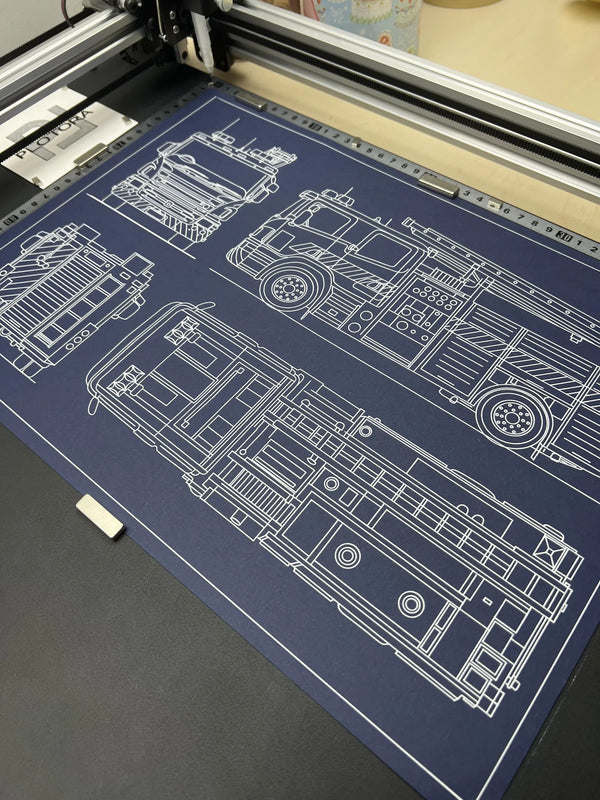 Fire truck blueprint being drawn by a pen plotter in white ink on navy blue paper, showing side, front and top views
