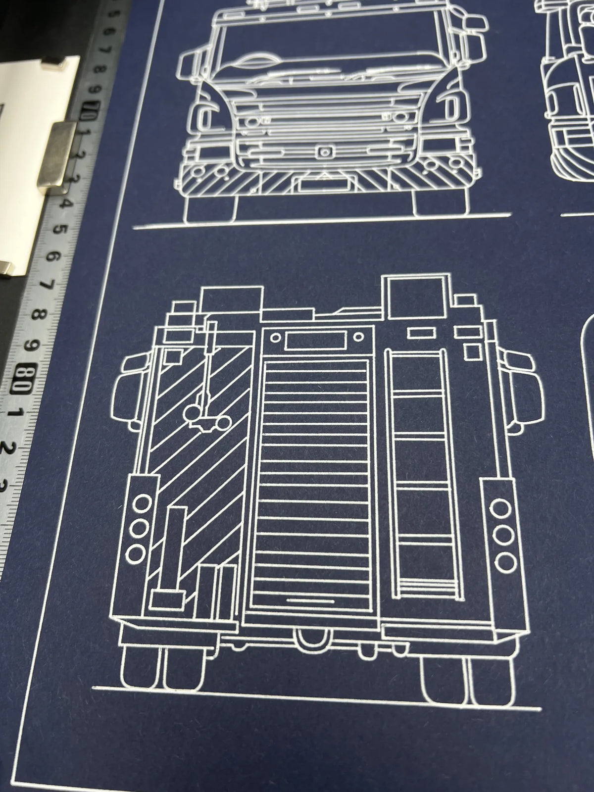 Front and rear views of a fire engine in a hand-plotted blueprint, white ink on navy paper with ruler for scale