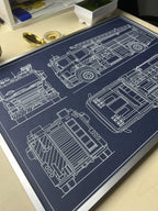 Fire truck blueprint art in a silver metal frame, displayed on a desk with a brass compass