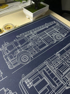 Close-up of framed fire engine blueprint showing side view with ladder and wheels, white line drawing