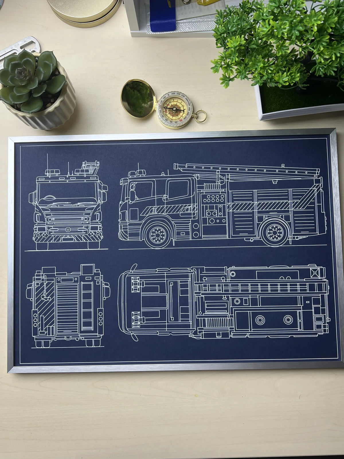 	Framed fire truck blueprint poster in silver metal frame on a desk, custom pen plotter wall art by Plotora