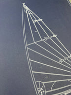 A close-up of a dark navy blue print or surface featuring a white line drawing of a sailboat rigging diagram.