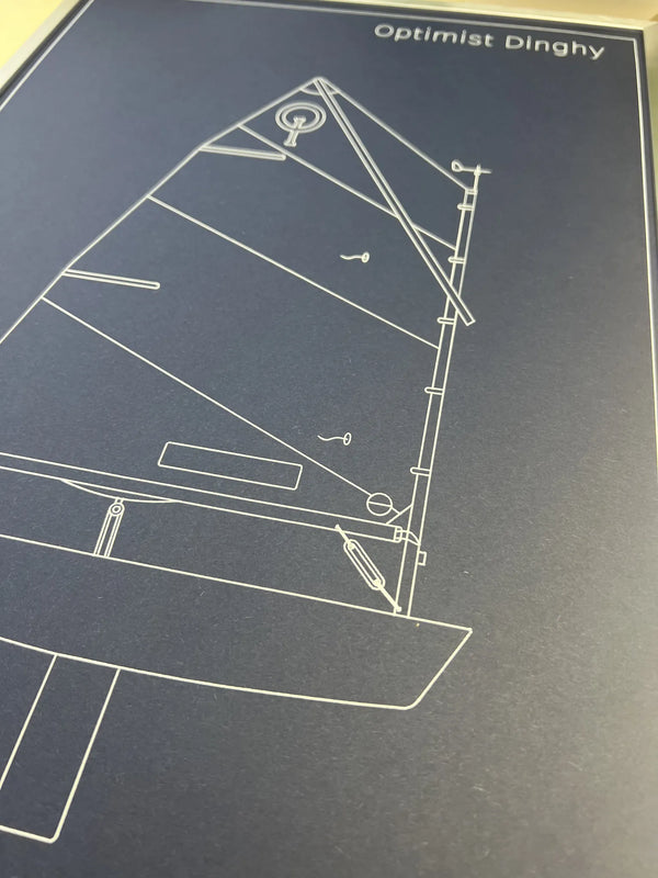 A close-up of a dark blue print or poster featuring a white line drawing of a sailboat and the text 'Optimist Dinghy' at the top.